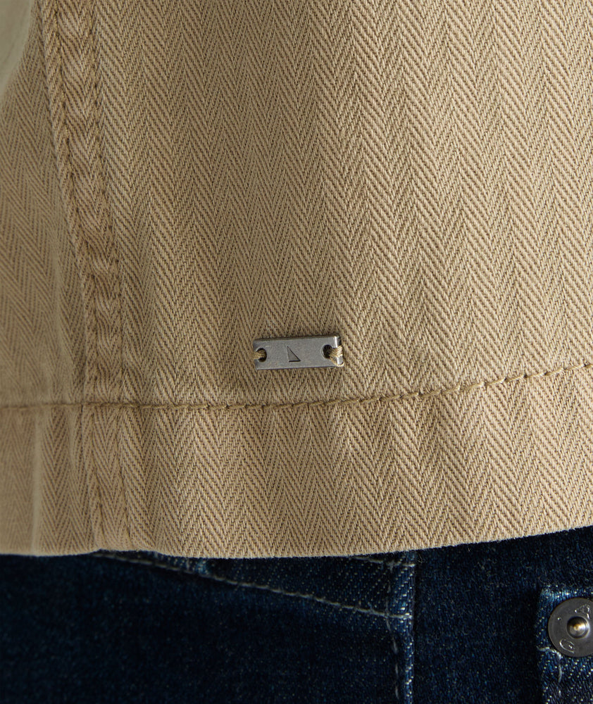 Model is wearing UNTUCKit chadwick herringbone over shirt in tan. 