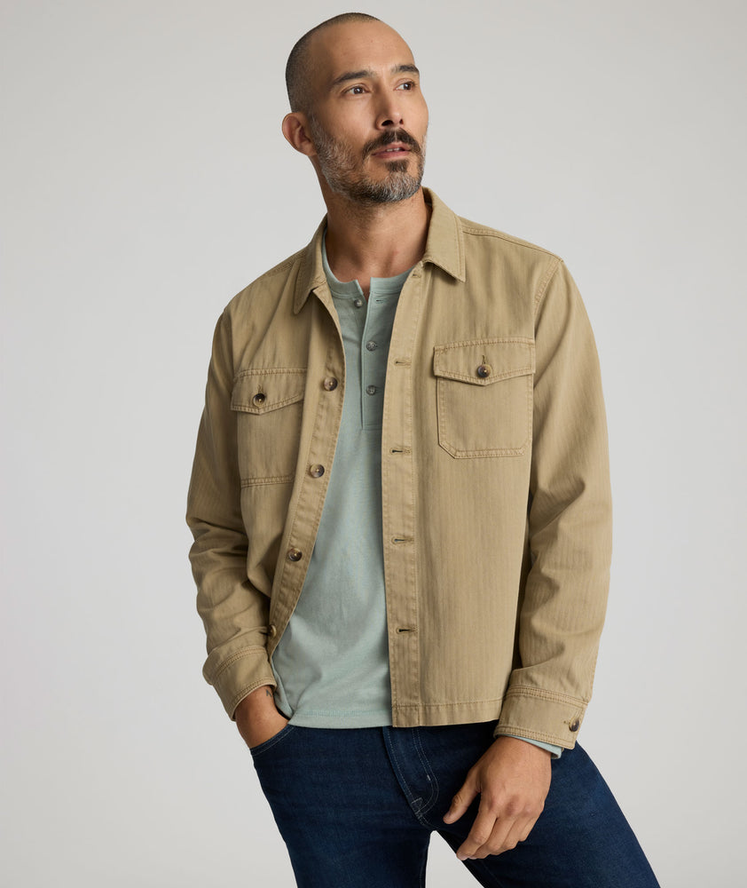 Model is wearing UNTUCKit chadwick herringbone over shirt in tan. 