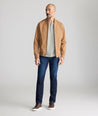 Man wearing a tan jacket, gray shirt, and blue jeans on a plain background