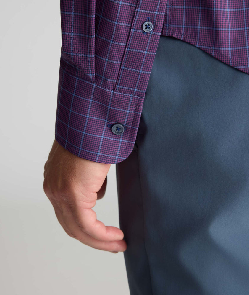 Close-up of a person wearing a purple and blue plaid button-down shirt with dark gray trousers, showing the cuff and hand.