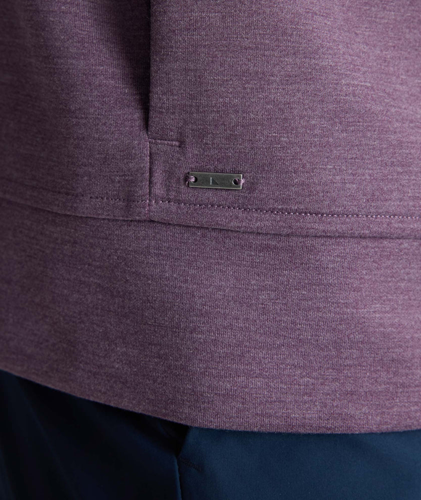 Close-up of a heathered purple athletic jacket showing the curved hem, a vertical seam, and a small rectangular metal brand plaque.