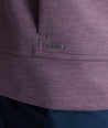 Close-up of a heathered purple athletic jacket showing the curved hem, a vertical seam, and a small rectangular metal brand plaque.